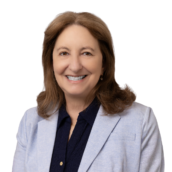 Professional headshot of woman with brown hair in light blue blazer and navy blouse.