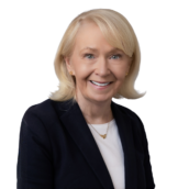 Professional headshot of a woman with blonde shoulder-length hair wearing a dark blazer and gold jewelry